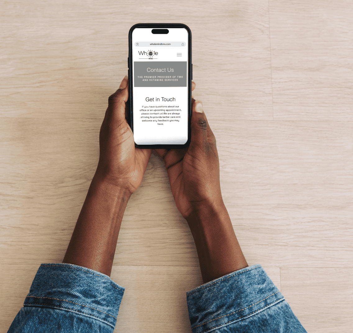 Hands holding smartphone with Whole Mind contact info