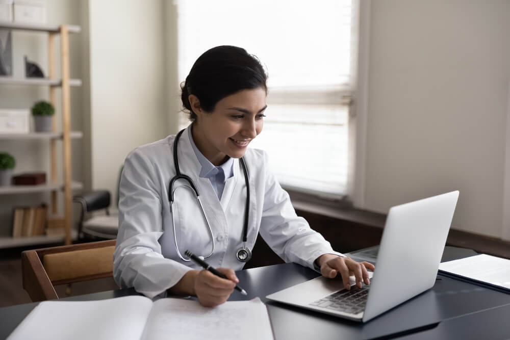 Happy young female physician working on computer
